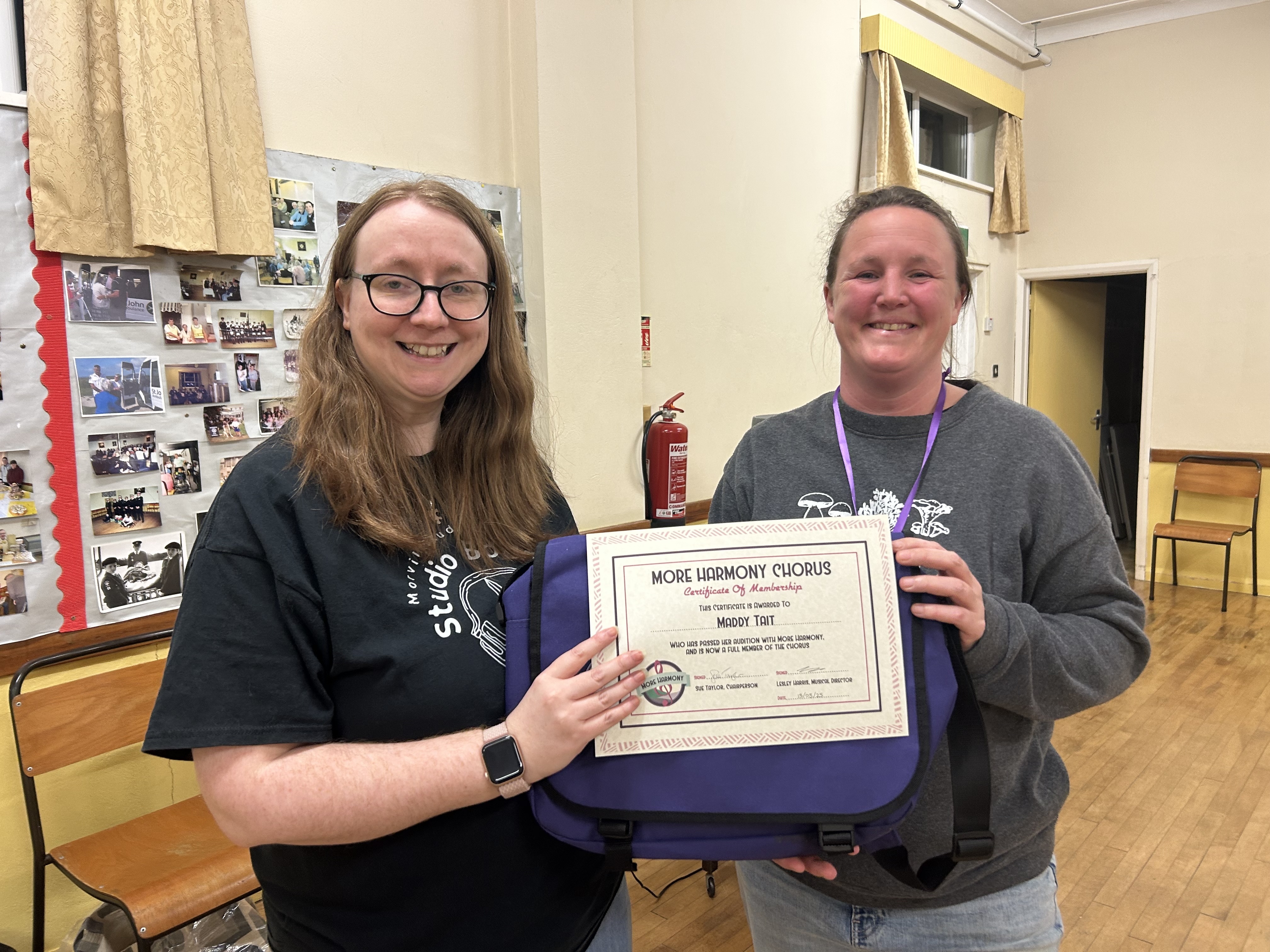 More Harmony Women's Barbershop Chorus MD Lesley hands new bass section member Maddy her membership certificate