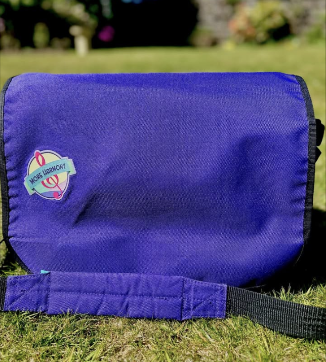 A close up of a purple More Harmony music bag in a pretty garden